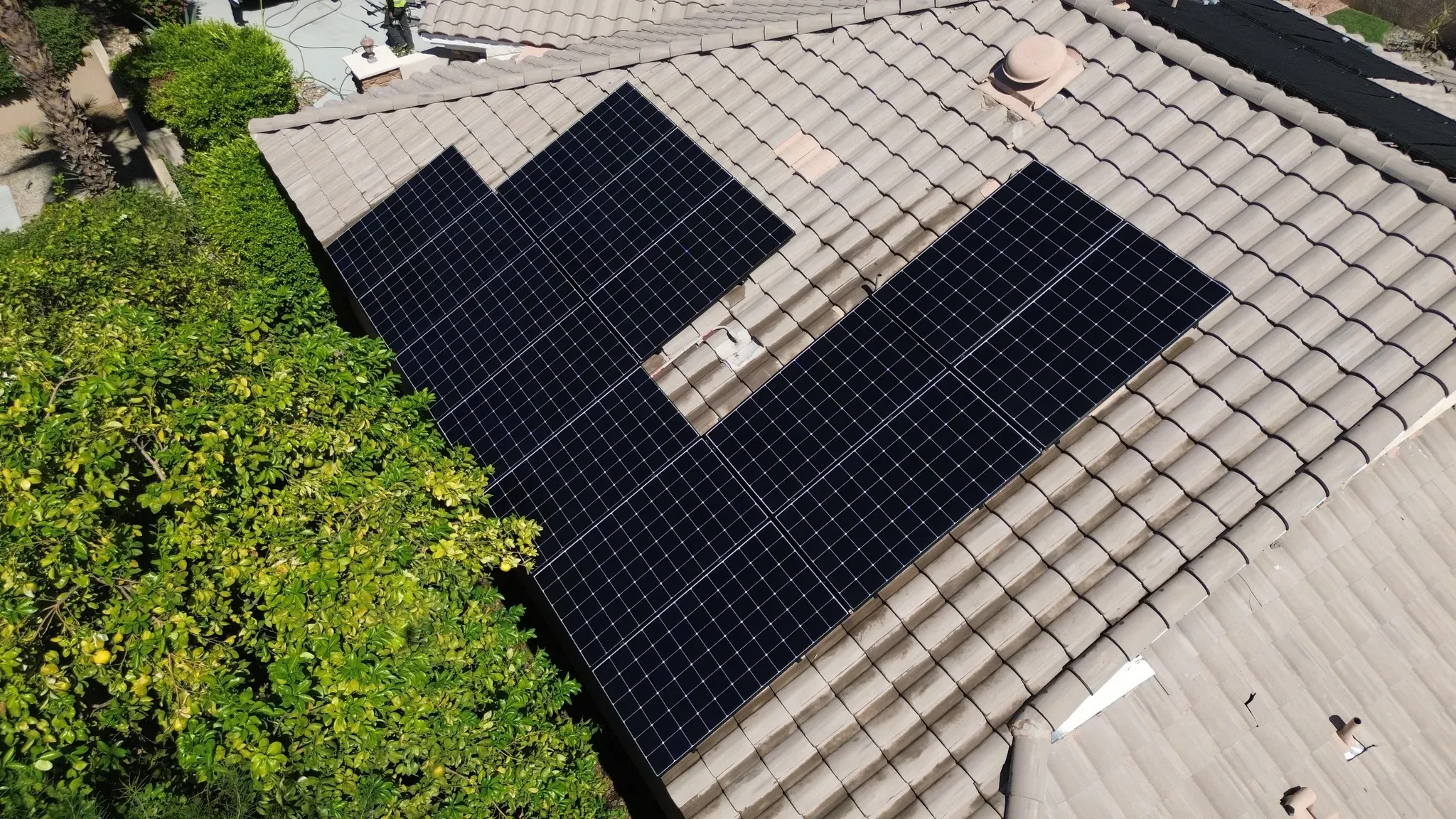 The same L-shaped solar array on a concrete tile roof clean and dark after a DronePower1 drone cleaning