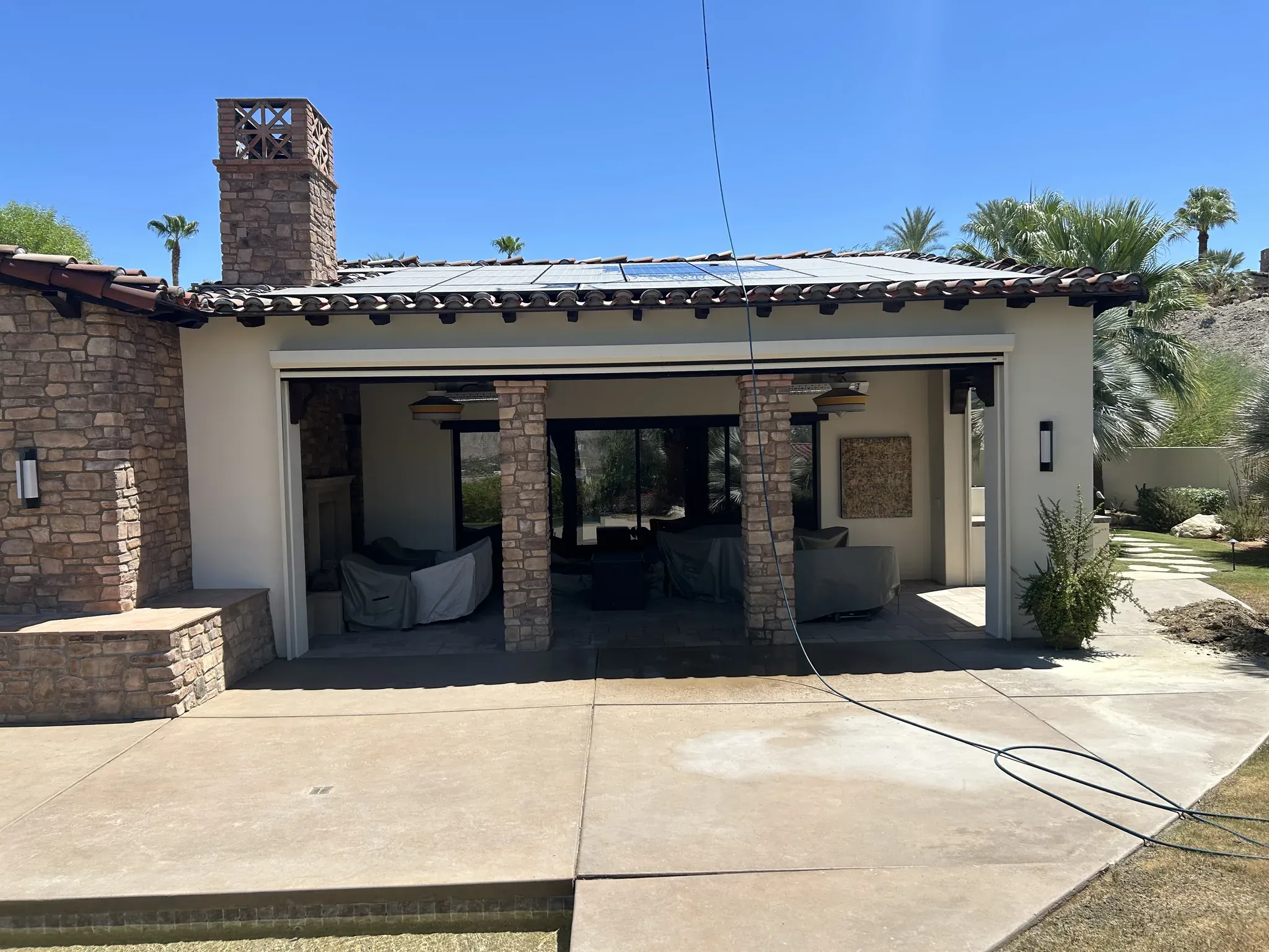 Rooftop solar panels on a Spanish tile roof dulled by a film of desert dust before a DronePower1 drone cleaning, with the water line staged on the dry patio below