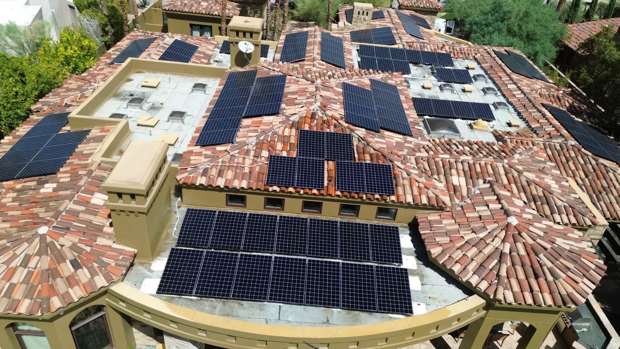 High-angle drone view of a large Spanish tile-roof estate with solar arrays spread across its tile slopes and flat roof sections