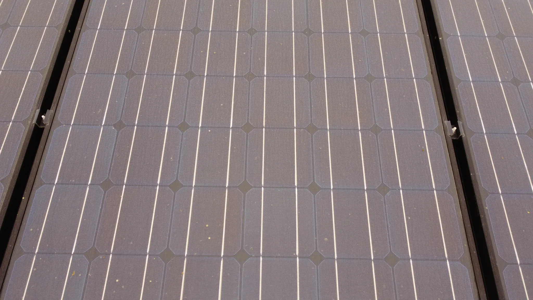 Close-up drone view of solar cells on the same San Diego North County tile roof, dulled by a layer of dust and scattered debris