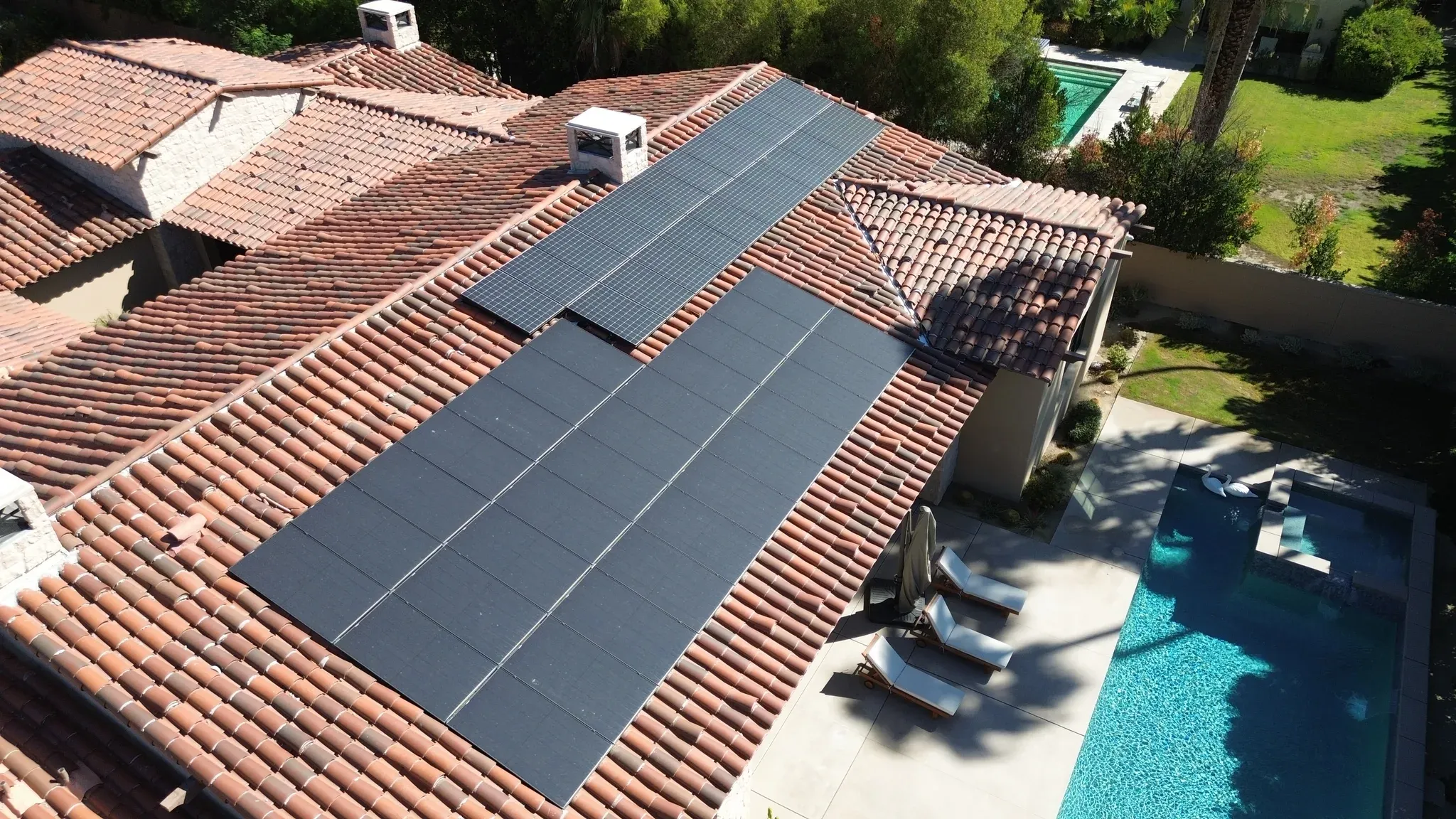 Drone view of a Coachella Valley Spanish tile-roof home with dust-dulled solar arrays above the backyard pool before a DronePower1 cleaning