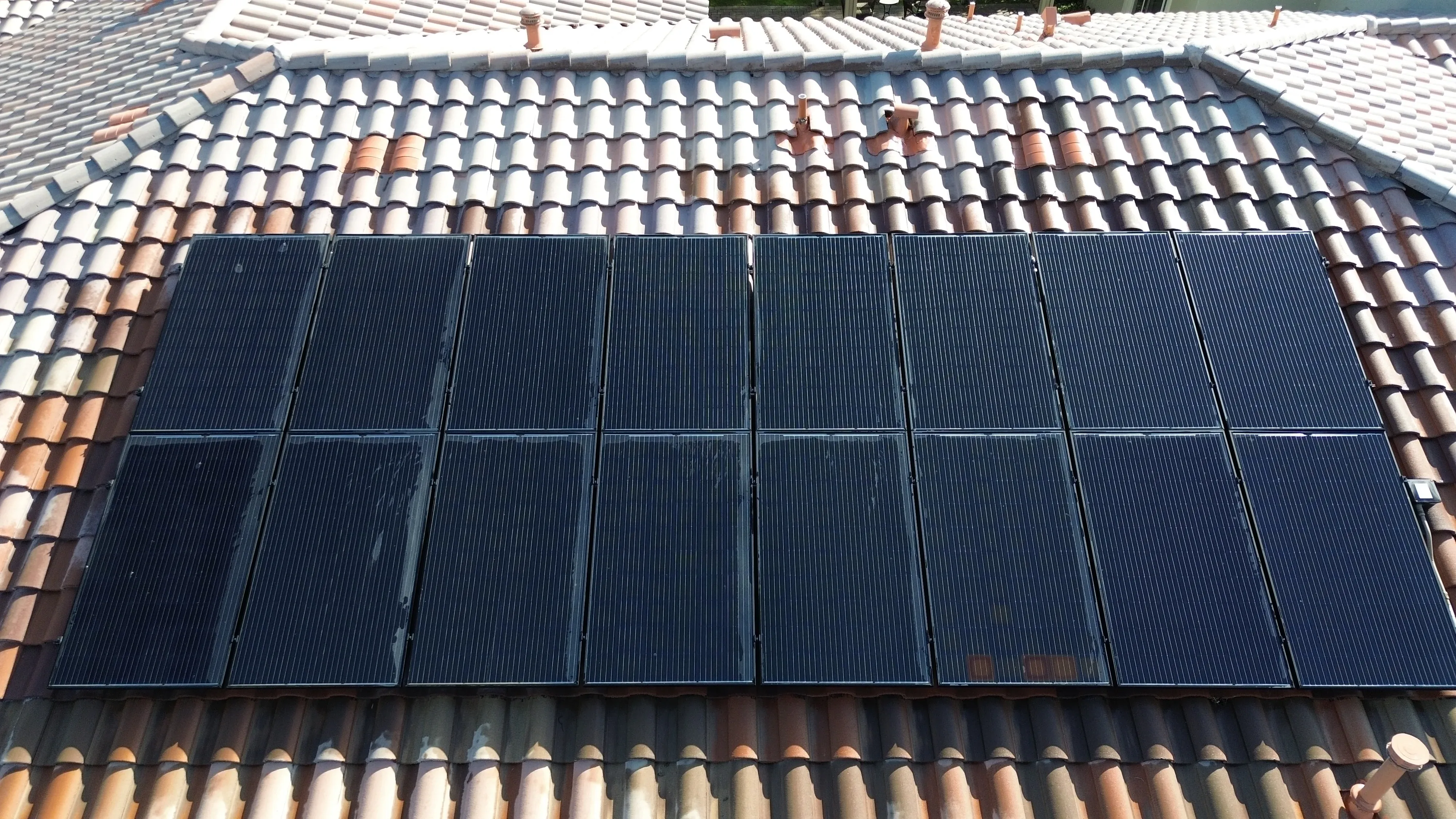 Rooftop solar array with a light film of desert dust on panels installed above clay tile roofing