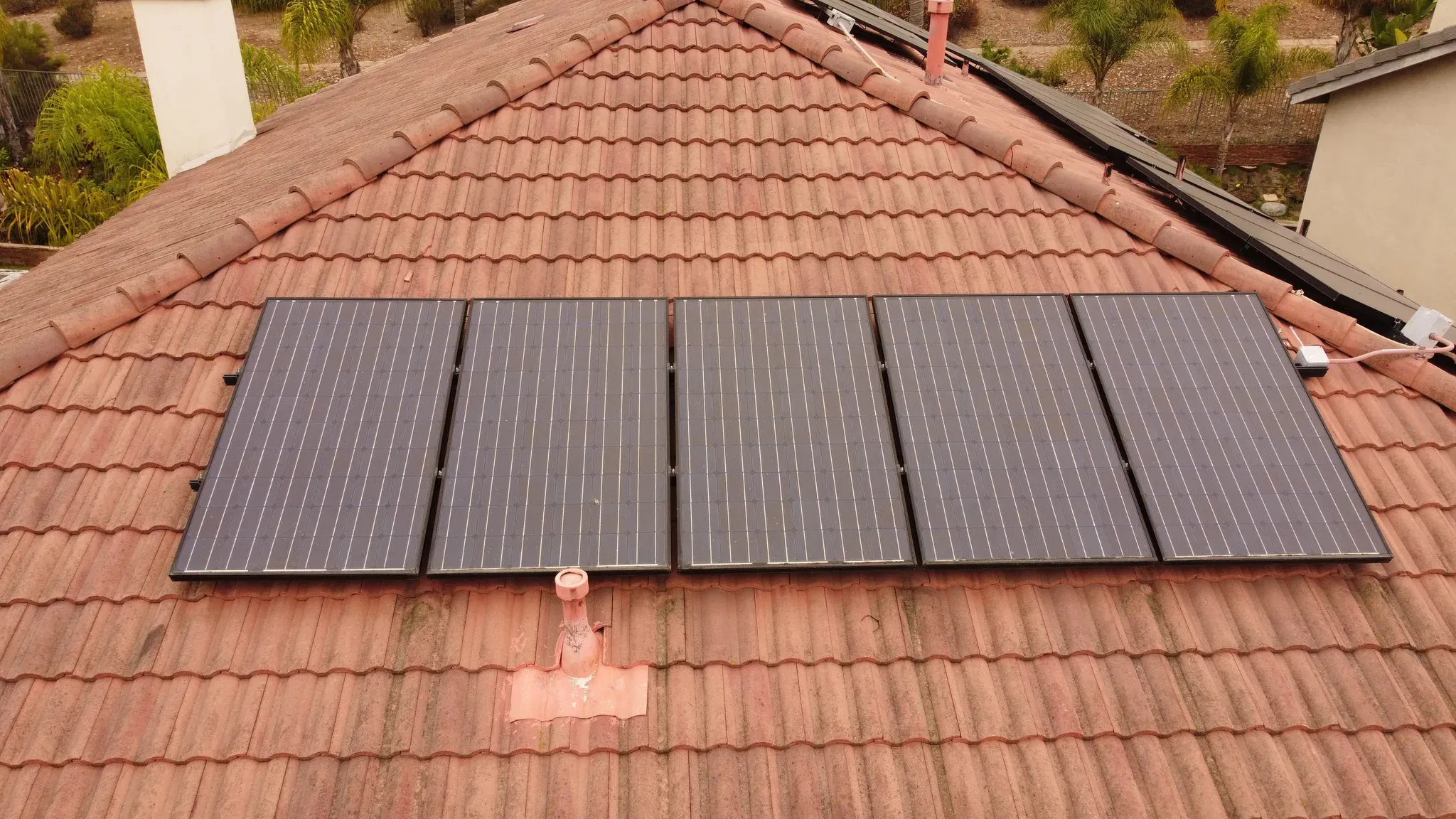 Drone view of five dusty solar panels mounted across a pitched terracotta tile roof in San Diego North County